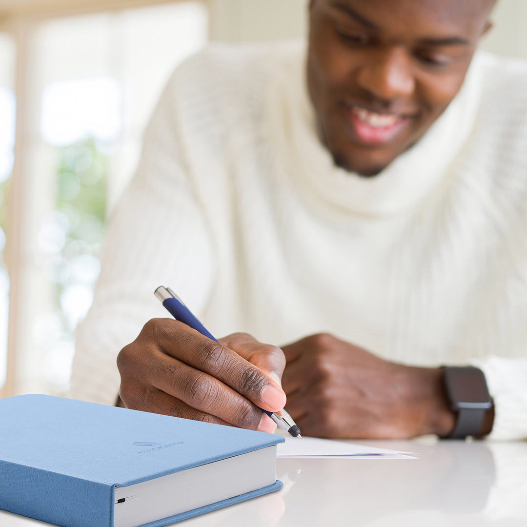 Image shows a man writing and a Multiplanner on the desk next to him