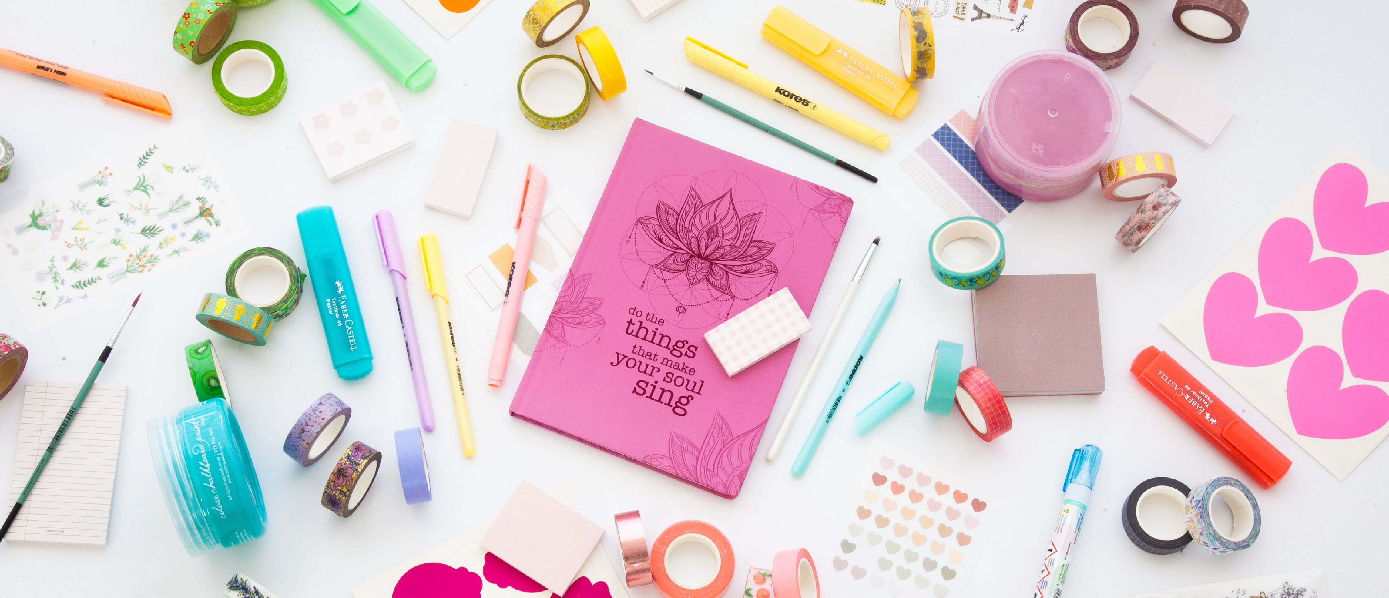 Image shows a pink journal with various stationery on a desk