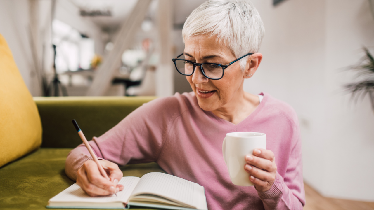 Mature lady sitting on the floor writing in her journal with a cup of tea