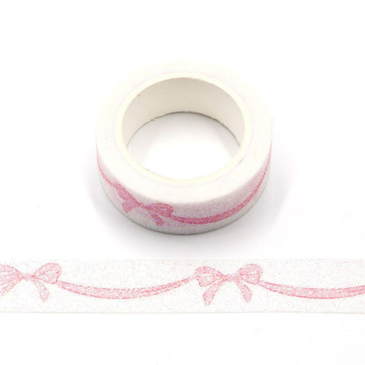 Roll of pink decorative  washi tape with a bow design on a white background
