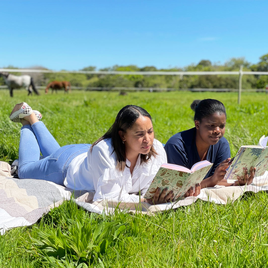 Image shows women laying in a field with diaries in hand